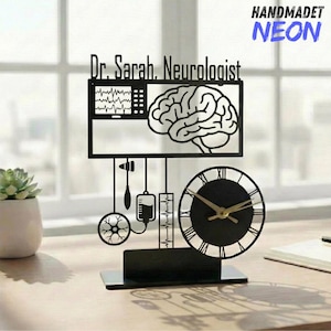 Puede incluir: Reloj de escritorio de metal negro con un diseño de cerebro y herramientas médicas. El reloj tiene una esfera redonda con números romanos y manecillas doradas. El nombre "Dr. Sarah, Neurologist" se muestra encima de la ilustración del cerebro. También se muestra la palabra "HANDMADET NEON".