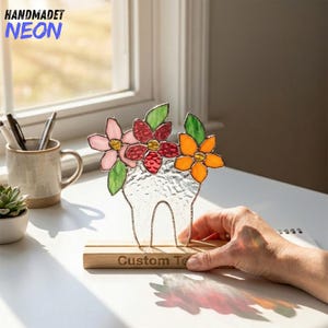 May include: A stained glass tooth sculpture with pink, red, and orange flowers and green leaves. The sculpture sits on a wooden base with the text "Custom Te". The word "HANDMADET NEON" is in the upper left corner.