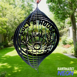 May include: Black metal wind spinner with the text "Lucy's House" and a seashell design. The wind spinner is hanging from a hook in a garden setting.