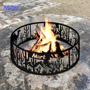 May include: A black metal fire pit with a desert cactus design and the name "Mark" cut out. The fire pit is circular and contains a burning fire. The text "HANDMADET NEON" is in the upper left corner.