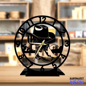May include: Black metal clock with a cowboy hat and boots design. The clock face has Roman numerals and a gold-colored hand. The clock is on a black stand.