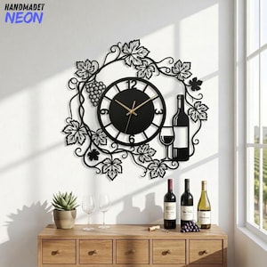 May include: A black metal wall clock featuring a circular face with gold hands, surrounded by a decorative frame of grapevines, grape clusters, a wine bottle, and a wine glass. The clock displays numbers 3, 6, 9, and 12 in a bold font.