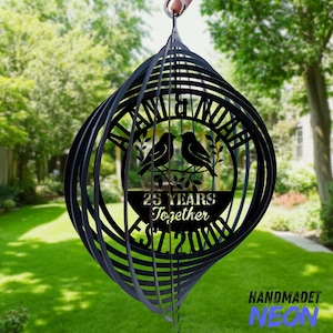 Pode incluir: Moinho de vento de metal preto com design em espiral. O centro apresenta dois p&aacute;ssaros num galho, o texto "25 YEARS Together EST 2000" e os nomes "ALAN & NOAH". O moinho de vento est&aacute; pendurado ao ar livre em frente a um gramado verde.