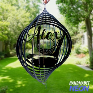 May include: Black metal wind spinner with a golf club and ball design. The name "Alex" is written in a decorative font on the spinner.
