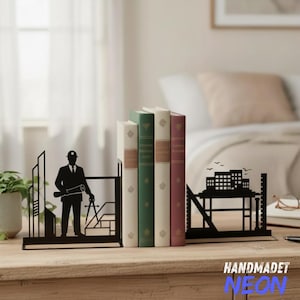 May include: Black metal bookends with an architect design, holding a row of books. The bookends feature a silhouette of a building and an architect with a blueprint and compass. The books are in shades of white, green, and burgundy.