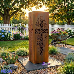 May include: A tall, rectangular, weathered metal garden sculpture featuring a cross design with rose and floral cutouts. The sculpture stands on a stone base in a garden setting, surrounded by plants, flowers, and a white picket fence.