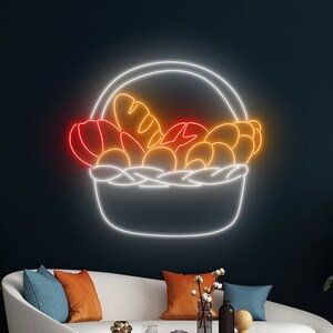 May include: A neon sign depicting a white wicker basket filled with orange and red fruit and bread. The basket is outlined in white and the fruit and bread are outlined in orange and red.