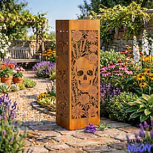 May include: A tall, rectangular, weathered metal garden sculpture with cut-out skull and floral designs. The sculpture is in a garden setting with flowers and a stone pathway. The metal has a rusty brown color.