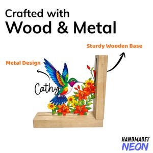 May include: A wooden and metal hummingbird design with a sturdy wooden base. The colourful hummingbird is surrounded by flowers and the name "Cathy". The text "Crafted with Wood & Metal" is at the top.