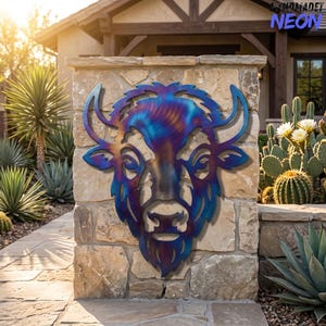 May include: A metal wall art piece shaped like a bison head, featuring a heat-treated finish with iridescent blue, purple, and bronze tones. The cutout design highlights the animal's horns, facial features, and shaggy mane in a stylized form.