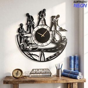 May include: A black metal wall clock featuring a construction theme with silhouettes of workers, a road roller, an excavator, and tools. The circular clock face has gold hands and numbers 3, 6, 9, and 12. The text HANDMADET NEON appears in the top right corner.