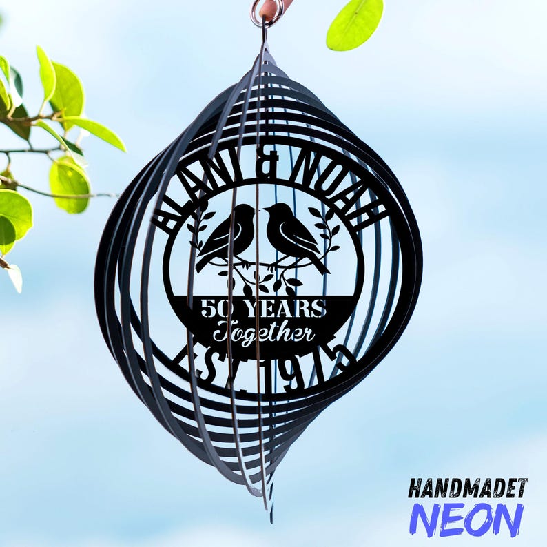 May include: Black metal wind spinner with a circular design featuring two birds, the text "BLAN & NOAH", and "50 YEARS Together". The bottom of the spinner has the text "ST 1974". The word "HANDMADET" is above the word "NEON".