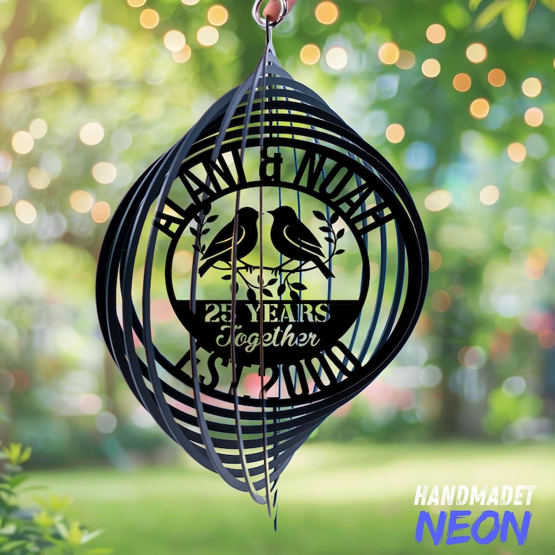Pode incluir: Catavento de metal preto com design em espiral. O centro apresenta um design circular com dois p&aacute;ssaros, os nomes "BLAN & NOAH", e o texto "25 YEARS Together" e "Since 2000". O canto inferior direito tem o texto "HANDMADET NEON".