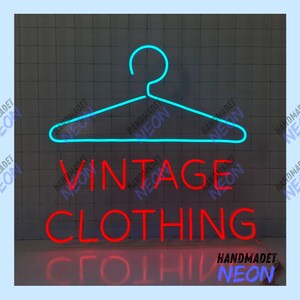Może przedstawiać: Neonowy znak w kolorze niebieskim w kształcie wieszaka na ubrania z napisem "Vintage Clothing" w kolorze czerwonym poniżej. Znak znajduje się na czarno-białym tle z płytek.