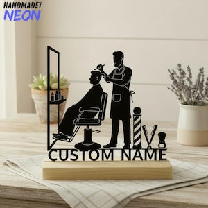 Puede incluir: Decoración de barbería en silueta negra con un barbero cortando el pelo a un cliente. El diseño incluye una silla de barbero, un espejo y herramientas, sobre una base de madera. El texto "CUSTOM NAME" se muestra debajo. El texto "HANDMADET NEON" está en la esquina superior izquierda.