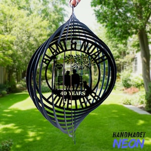 Puede incluir: Molinillo de viento de metal negro con diseño en espiral. El centro presenta una silueta de una pareja en un banco con un perro, bajo un árbol, con las palabras "Alan & Noah" y "40 Years Together."