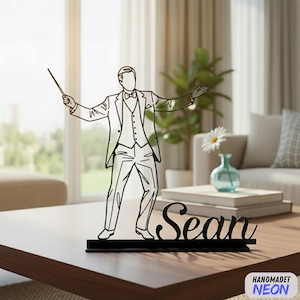 Könnte beinhalten: Eine schwarze, lasergeschnittene Silhouette eines Dirigenten im Smoking, der einen Taktstock hält und mit den Armen gestikuliert. Der Name "Sean" wird in Schreibschrift angezeigt. Die Basis ist schwarz, und der Hintergrund zeigt ein Wohnzimmer.