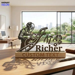 May include: A dark metal cutout sign featuring a welder in a helmet, tools, and gears, with the name "Richer" and the text "CUSTOM TEXT" engraved on a rectangular wooden base. The design includes a stylized arc welding spark effect.