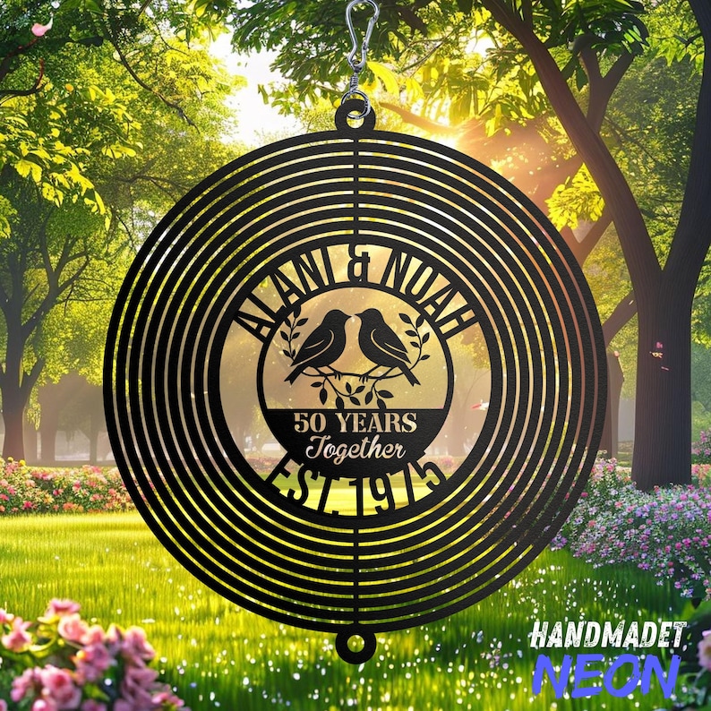May include: A black metal wind spinner with a circular design. The center features the names "ALANI & NOAH", two birds on a branch, and the text "50 YEARS Together EST. 1975". The spinner hangs from a silver hook.