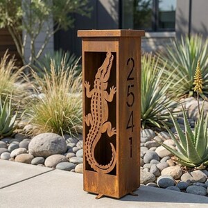 Puede incluir: Un poste de dirección alto y rectangular de metal color óxido que presenta una silueta de caimán cortada con láser en el panel frontal y los números de casa 2541 dispuestos verticalmente en una fuente sans-serif en el panel lateral.
