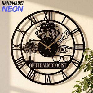 May include: A black circular wall clock featuring Roman numerals and a central design related to ophthalmology. The clock face includes silhouettes of a phoropter, an eye, and eyeglasses, with the word OPHTHALMOLOGIST printed at the bottom.