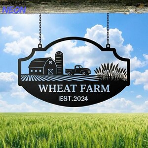 Peut inclure: Panneau de ferme de blé en métal noir avec une silhouette de grange, de silo et de camion. Le panneau comprend le texte "WHEAT FARM" et "EST. 2024" sur fond de blé et de ciel bleu. Le panneau est suspendu par des chaînes.