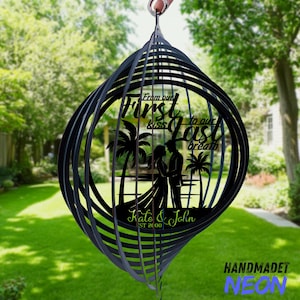 May include: Black metal wind spinner with a romantic design. The spinner features a silhouette of a couple, palm trees, and the text "From our first kiss to our last breath." The names "Kate & John" are also included.