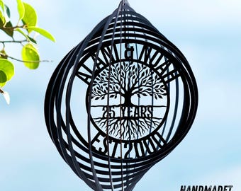 Könnte beinhalten: Ein schwarzer Windspinner aus Metall mit einem kreisförmigen Zentrum und einem lasergeschnittenen Baummotiv. Der Text ALAN & NOAH steht oben, 25 YEARS in der Mitte und EST. 2000 unten. Die äußeren Ringe bilden eine sphärische Form.
