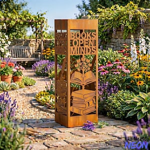 May include: A rectangular, weathered metal garden sculpture with cut-out designs of books, a tree, and the words "BOOKS OPEN MINDS." The sculpture is placed in a garden setting with flowers and a brick pathway.