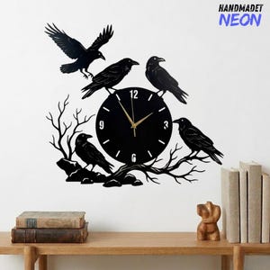 Puede incluir: Reloj de pared de metal negro con esfera circular y agujas doradas. Cuatro siluetas de cuervos están posadas en el reloj y ramas. El texto "HANDMADET NEON" está en la esquina superior derecha.