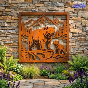 May include: A square metal wall art panel featuring a laser-cut design of a large bear and a cub standing on a rocky outcrop. The scene includes a forest of pine trees and mountain peaks in the background. The metal has a rusted, orange-brown finish.