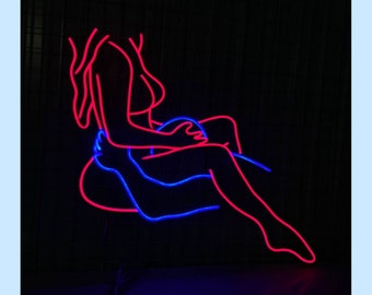 Pode incluir: Placa de néon que representa duas figuras em um abraço romântico. A figura feminina está em néon rosa e a figura masculina em néon azul.