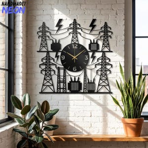 May include: A black wall clock featuring a laser-cut design of electrical transmission towers, power lines, and transformers. The circular clock face is centered within the metal structure, displaying gold hands and white numerals at 3, 6, 9, and 12.