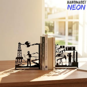 May include: A pair of black metal bookends featuring intricate laser-cut silhouettes of oil industry scenes. One piece depicts a worker with a blueprint near a derrick, while the other shows a worker observing oil pumps and storage tanks.