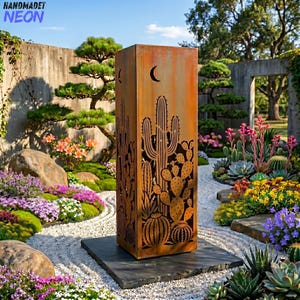 Puede incluir: Una escultura de jardín alta y rectangular de metal oxidado con un diseño de cactus. La escultura tiene un recorte de media luna y está colocada sobre una base de piedra gris oscuro. El fondo incluye un exuberante jardín con varias plantas y flores.