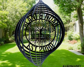 May include: A black metal wind spinner with a spherical, multi-layered design. The center features a laser-cut tree with roots and the text ALANI & NOAH, 30 YEARS, and EST 2000. The object is suspended by a small metal ring at the top.