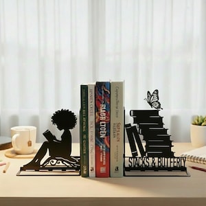 May include: Black metal bookends featuring a silhouette of a person reading and a stack of books with a butterfly. The bookends are holding several books. The text "STACKS & BUTTERFLY" is visible.