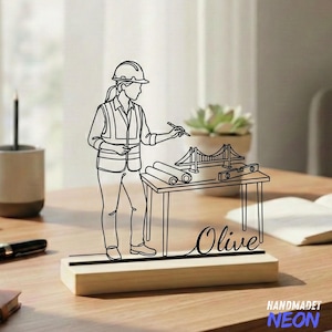 May include: A black line art engineer design on a wooden base. The design features an engineer with a hard hat, vest, and blueprints, with the name "Olive" in cursive. The base has the text "HANDMADET NEON" in blue.