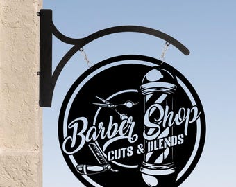 Può includere: Segno al neon bianco e nero con un palo da barbiere e il testo "Barber Shop Cuts & Blends". Il segno è appeso a una staffa di metallo nero.