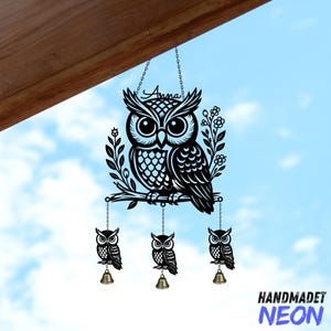 May include: Black metal owl wind chime with three smaller owl pendants, each with a bell. The main owl is perched on a branch with floral accents. The word "Anna" is written above the owl. The background is a blue sky.