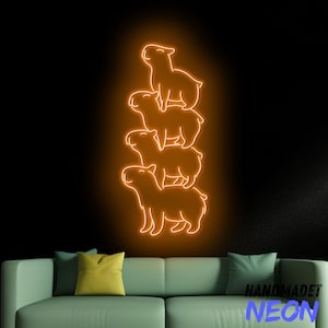 Könnte beinhalten: Ein Neon-Schild mit orangefarbenem Leuchten, das vier übereinander gestapelte Capybaras zeigt. Das Schild ist an einer dunklen Wand hinter einem grünen Sofa angebracht.