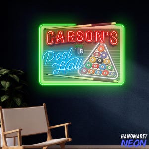 May include: Neon sign with the text "CARSON'S Pool Hall" in red and blue. The sign features a green border, a triangle of billiard balls, and two pool cues. The sign is mounted on a dark blue wall.