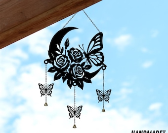 May include: Black metal moon-shaped wall hanging featuring roses, butterflies, and hanging butterfly charms. The design includes a crescent moon, three roses, and three butterflies. The butterflies hang from chains with small bells. The text "HANDMADET NEON" is in the bottom right corner.