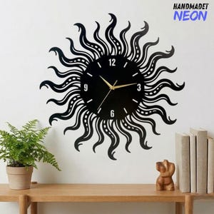 May include: Black sunburst-shaped wall clock with gold hands and a black face. The clock is mounted on a white wall. The text "HANDMADET NEON" is in the upper right corner. A small fern in a pot and decorative items are on a wooden shelf below.
