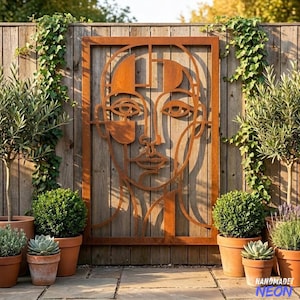 May include: A rectangular metal wall art piece featuring a stylised, abstract line-art portrait of a face. The artwork is constructed from rusted, weathered steel with a deep orange-brown patina, framed by a solid rectangular border.