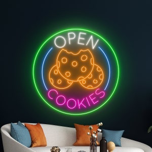 May include: Neon sign with a green circle and the words "OPEN COOKIES" in pink and white. Three orange cookies are inside the circle.