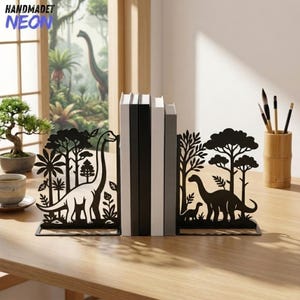 May include: A pair of black metal bookends featuring a laser-cut silhouette design of long-necked dinosaurs standing among trees and foliage. The bookends are positioned on either side of a row of books, creating a decorative display.