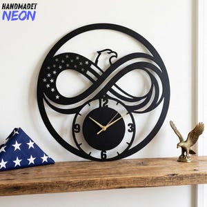 May include: Black metal wall clock featuring an eagle, American flag design, and an infinity symbol. The clock face is black with gold hands. The text "HANDMADET NEON" is in the upper left corner. A small gold eagle statue is on a wooden shelf.