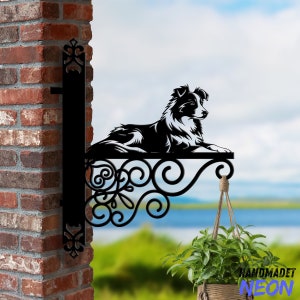 May include: Black metal wall-mounted sign featuring a silhouette of a border collie dog. The sign has a decorative scroll design and a hanging planter with green plants.