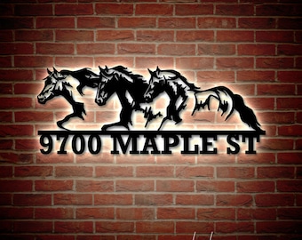 May include: Black metal house number sign with three horses running in front of a mountain range. The sign reads "9700 Maple St."